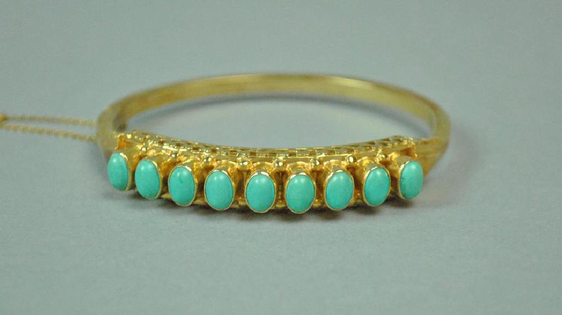 GOLD & TURQUOISE HINGED BANGLE: set with 9 (6x4mm) oval stones, height 10mm, interior 59x52mm, in yellow gold, safety chain, tongue stamped 585, 22.6gms.