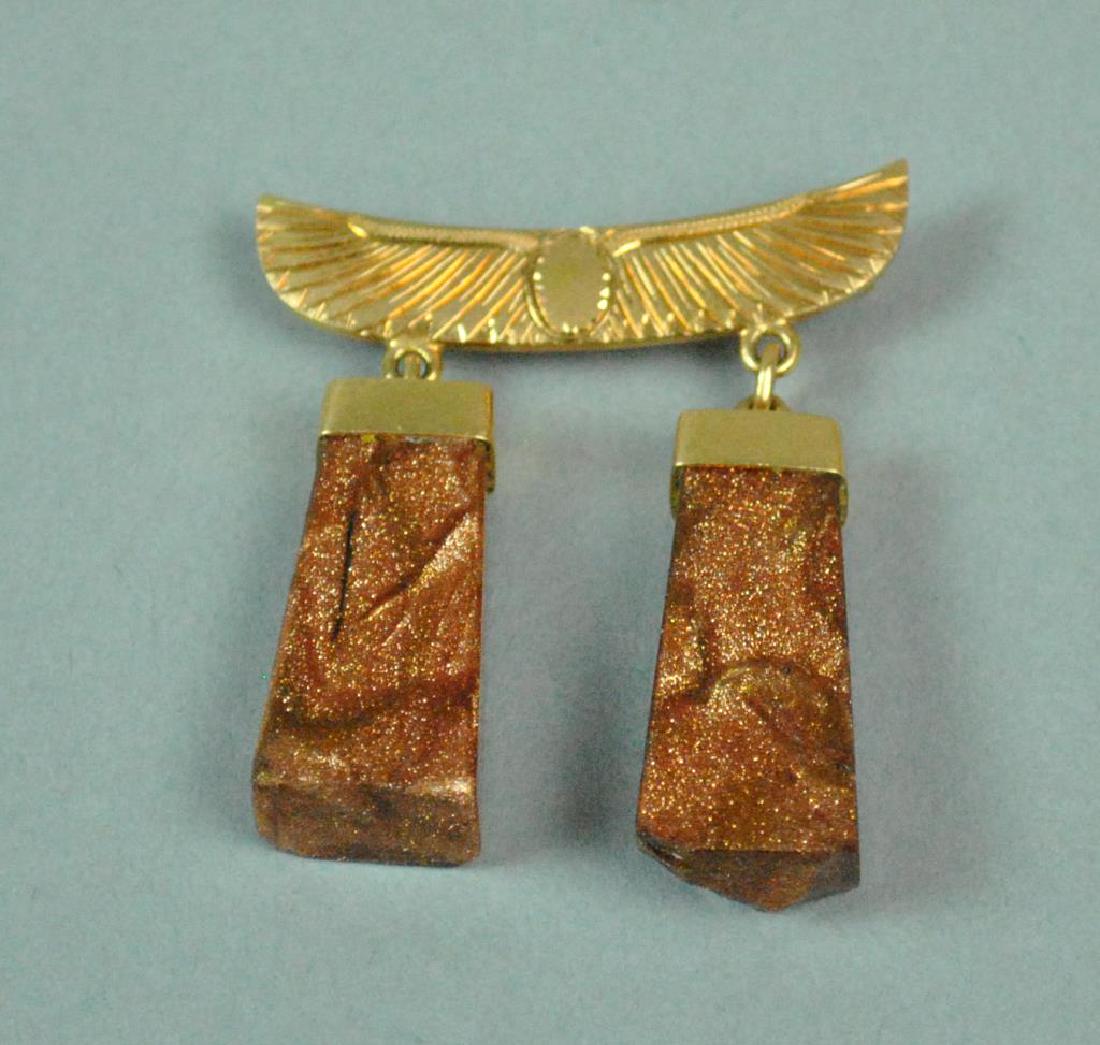22K EGYPTIAN GOLD MOUNTED GOLDSTONE DANGLING PIN: designed with winged solar disc suspending 2 obelisk style goldstones (stone chips, mainly to bottoms), tests 22K, wing width 1.5in., overall length 1.8in., 15.7gms.