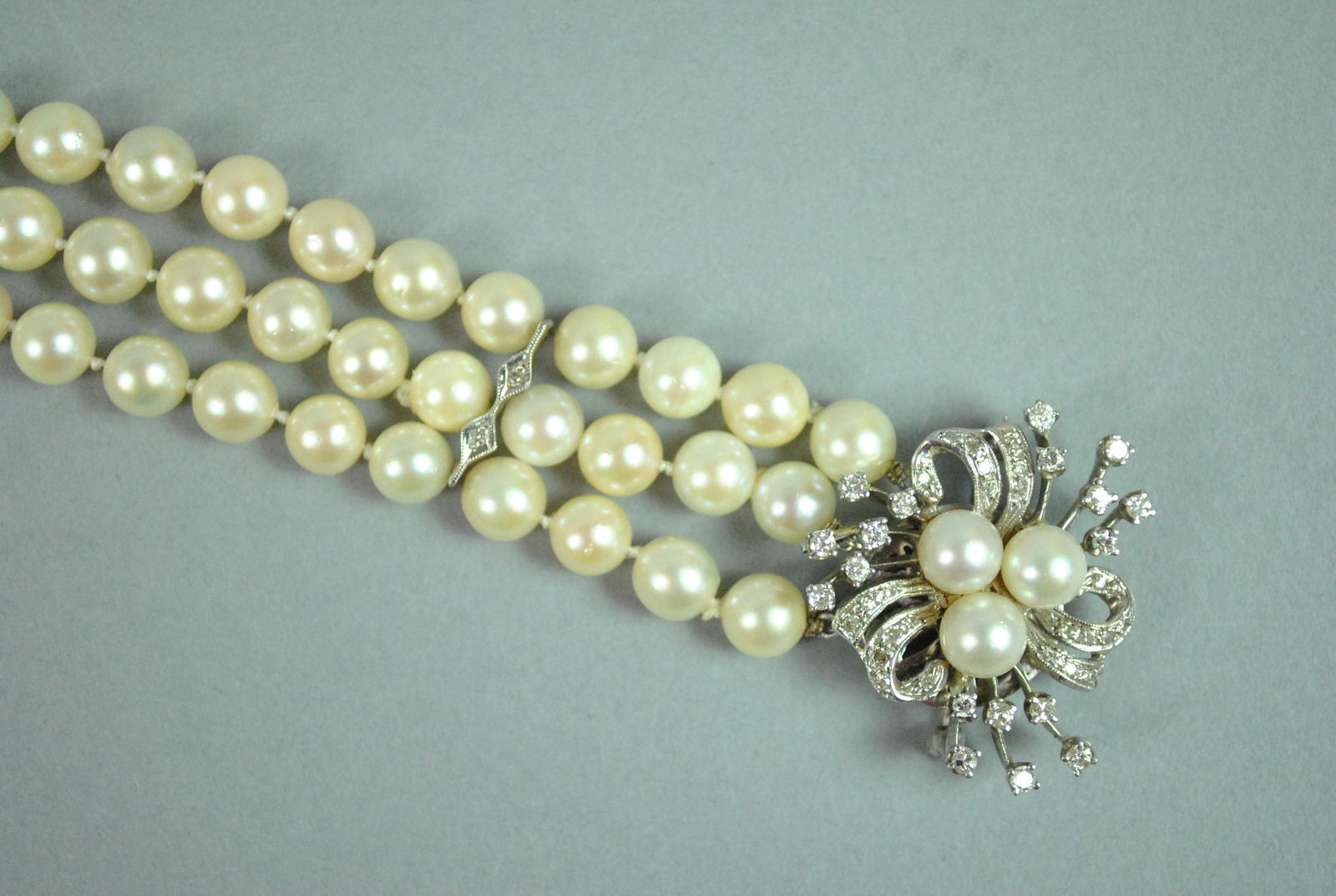 PEARL BRACELET W/DIAMOND BROOCH CLASP CONVERSION: PEARL BRACELET W/DIAMOND BROOCH CLASP CONVERSION the bracelet comprising 3 strands of (6.4-6.9mm) cultured pearls with 3 spacer bars each set with 2 diamond melee, tongue stamped 14K, safety catch, he