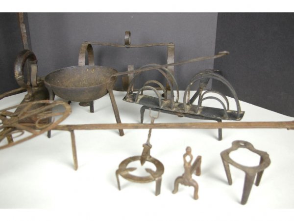 17-PIECE WROUGHT IRONWARE GROUP FOR THE HEARTH: including a 30" kettle stand, a rotating trivet, a swivel toaster, a pipe kiln, a spider pan, a chain trammel, an iron, a miniature andiron, trivets, tongs, etc., losses The Knoop Collection