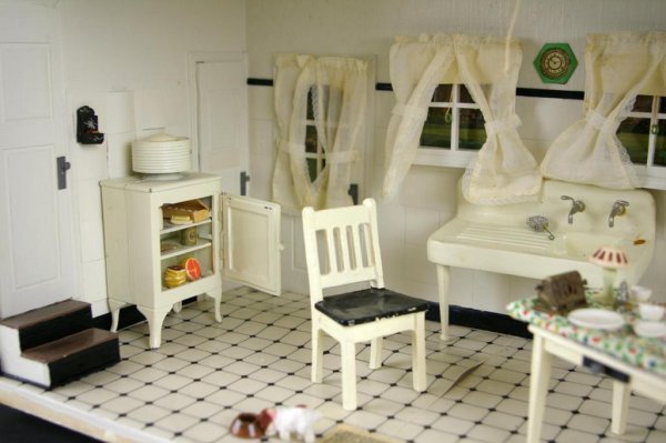 THE WELSH FAMILY KITCHEN DIORAMA: by Jeanne Knoop, with black and white tile floor, miniatures comprise vintage appliances including a sink with drain and a refrigerator stocked with food, linens, a meat grinder, dishes, toaster, etc.