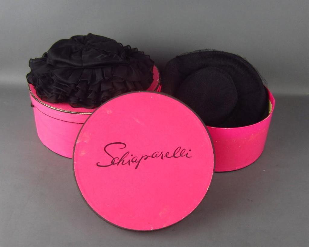 VINTAGE HATTIE CARNEGIE AND SCHIAPARELLI HATS: each in black, the Schiaparelli hat ruffled, the Hattie Carnegie hat with black mesh veil, each 12" diameter, each with labels, together with two Schiaparelli hat boxes (worn), largest diameter 14in.