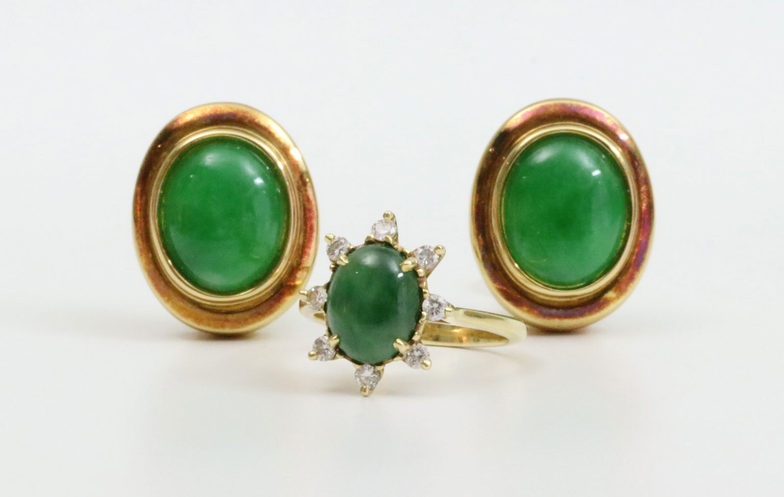 18K JADEITE GROUP - EARCLIPS AND A RING: the earrings each set with an oval jadeite stone approx. 11x9mm, overall 18x15mm, (gold surround with tarnish or darkening), omega backs, the ring set with a 9x7mm jadeite stone accented with 8 round