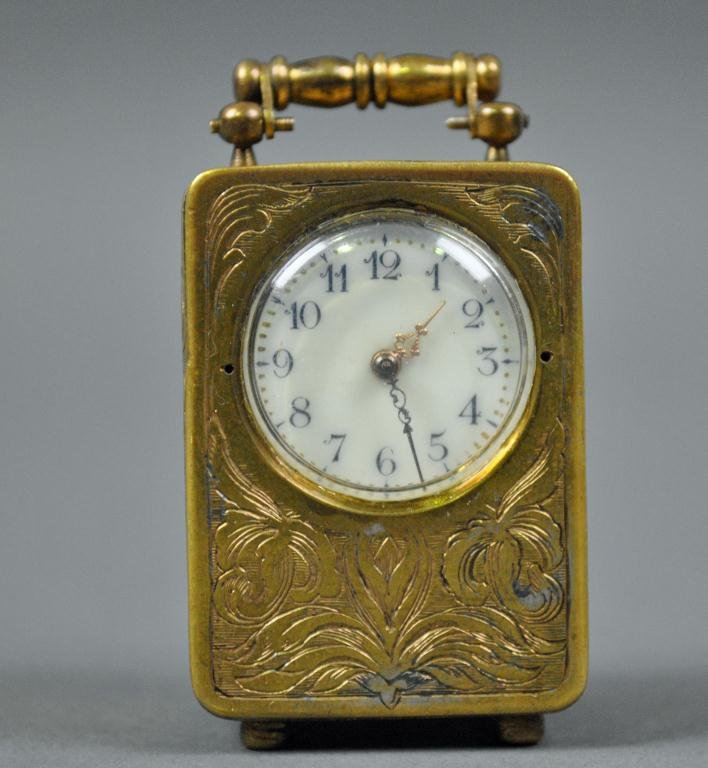 VACHERON & CONSTANTIN MINIATURE CARRIAGE CLOCK: the brass case with Art Nouveau engraved florals, Arabic numeral painted porcelain dial (hairline crack), swing handle, bun feet, works signed Vacheron & Constantin, 1.75in.