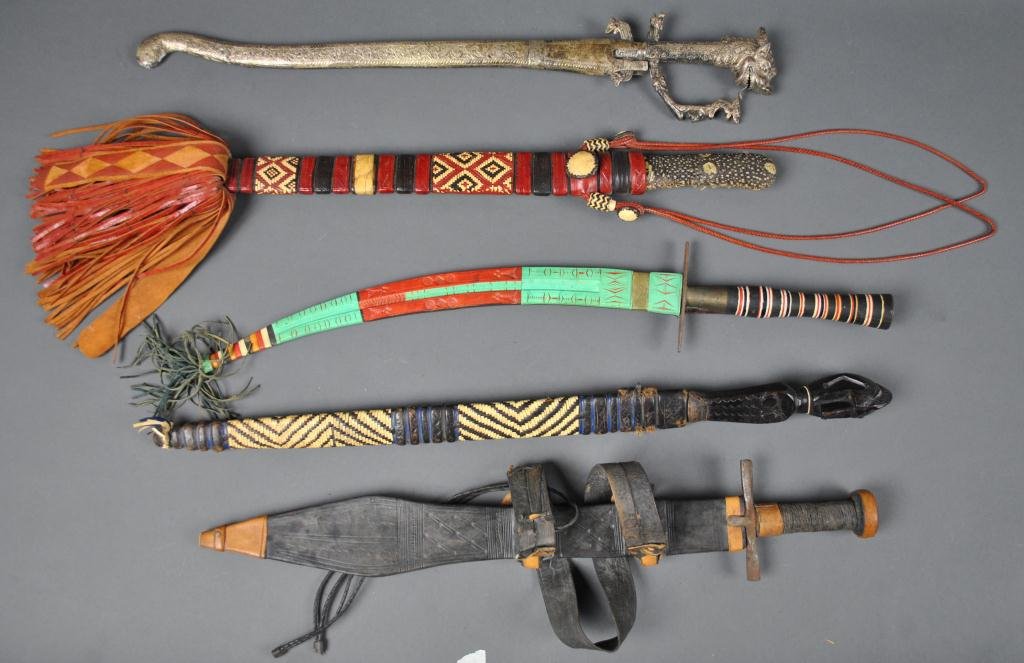 FIVE METAL EDGED ETHNOGRAPHIC WEAPONS: all with scabbards, four leather and one metal, one with wood carved figural and one with dragon-like handles, some rust and pitting, longest 26in.