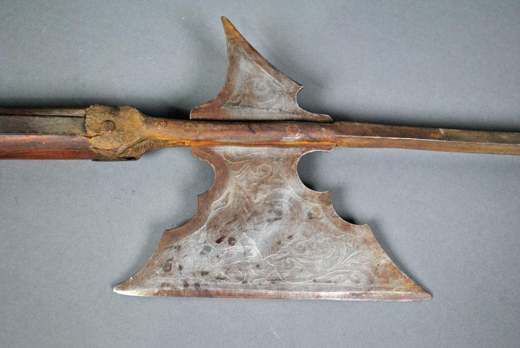 ETCHED IRON HALBERD: likely German, spiked axe blade with etched scrolls and helmet on one side, scrolls and shield on the other, replaced wood shaft, overall 83in.