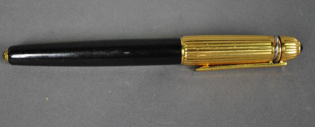 CARTIER PASHA LACQUER BALL POINT PEN: with black cylinder, a gold plated ribbed cap decorated with a trois-anneaux ring and a black cabochon terminal, signed Pasha de Cartier #9137, dated 1990, lacking a roller cartridge