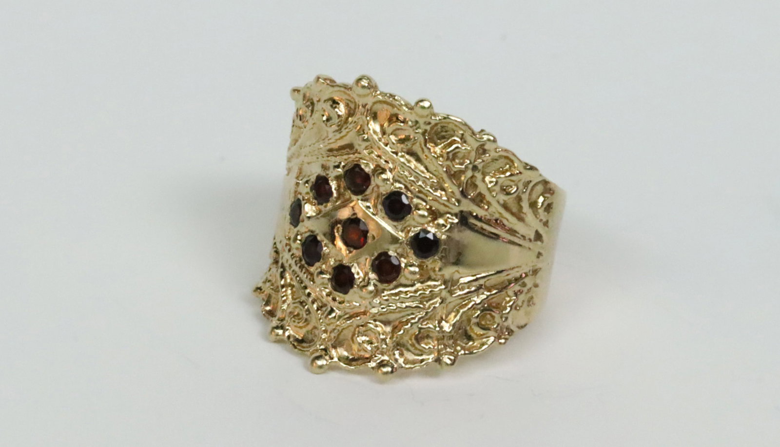 14K GARNET WIDE BAND RING: in carved yellow gold ornate design accented with 9 round garnets approx. 0.45ctw, stamped 14K, height 23mm, size 9.5, 10.2gms., Opening Bid $300
