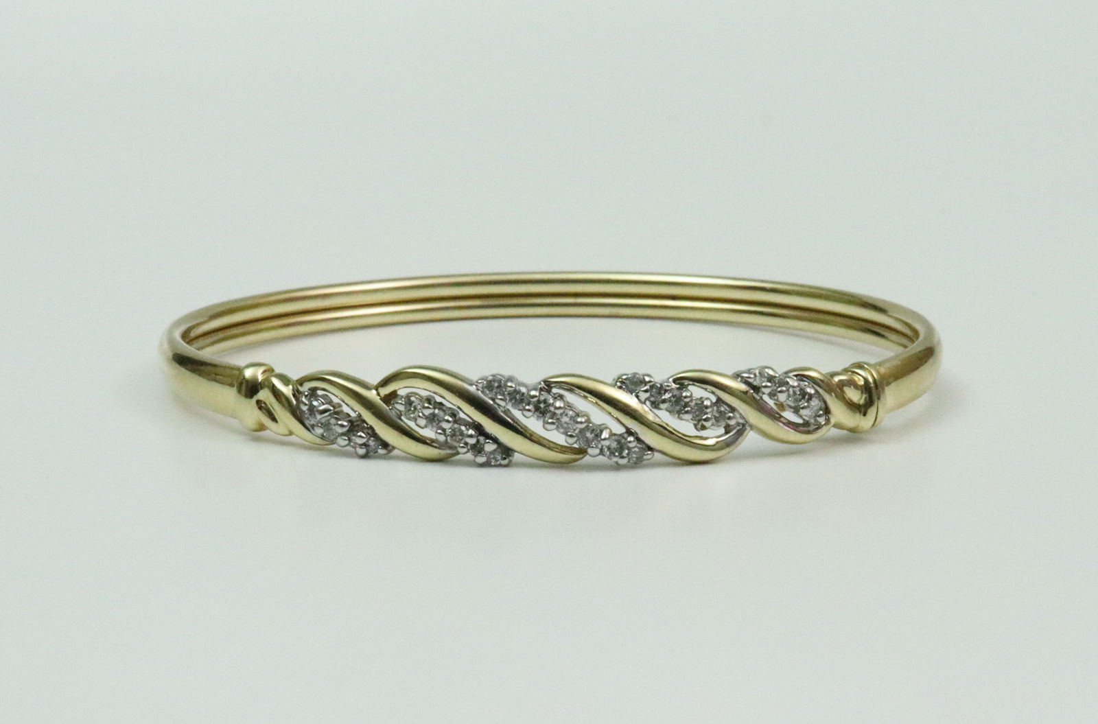 14K DIAMOND BANGLE: the scroll front design set with 25 round natural diamonds approx. 0.50ctw, front closure with safety catch, bracelet has some flexibility, front width 7mm, in yellow gold, stamped 14K, 7.8gms., Openi