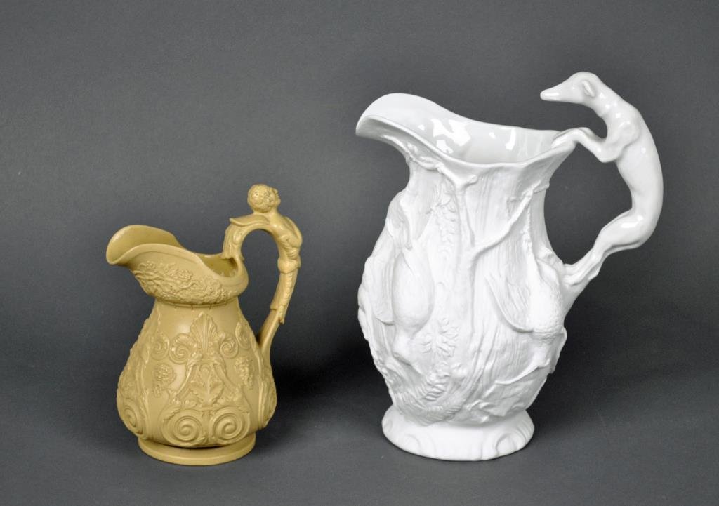 TWO COLLECTIBLE POTTERY PITCHERS: including a Parian hound-handled pitcher, and a footed salt-glaze wine pitcher with allover Bacchus masks and grape clusters, both with glazed interiors, tallest 11in.