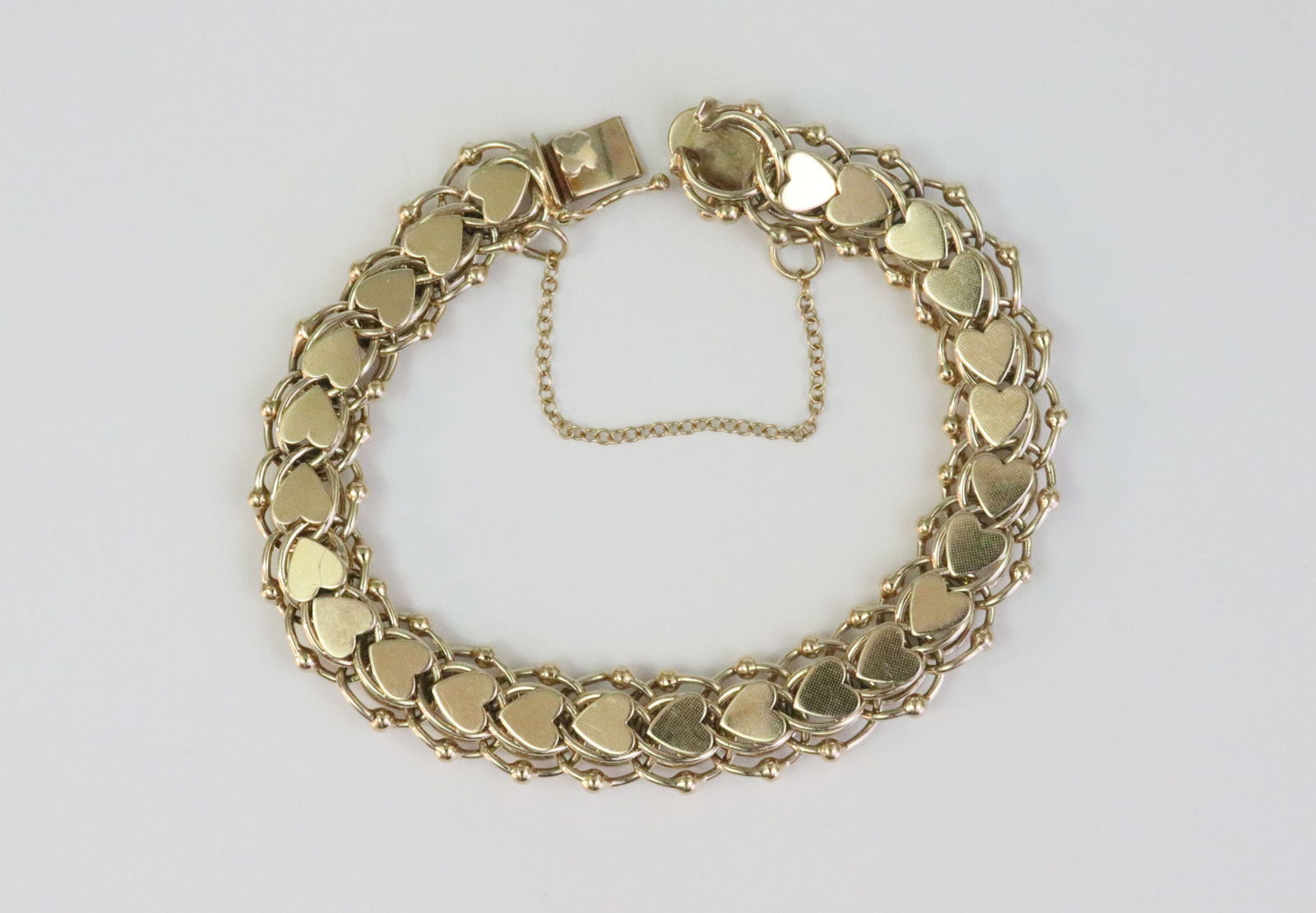 14K FANCY HEART LINK BRACELET: designed in parallel and heart link with bead trim, width 12mm, length 7.5in., stamped 14K, fixed safety chain, 26gms., Opening Bid $1300