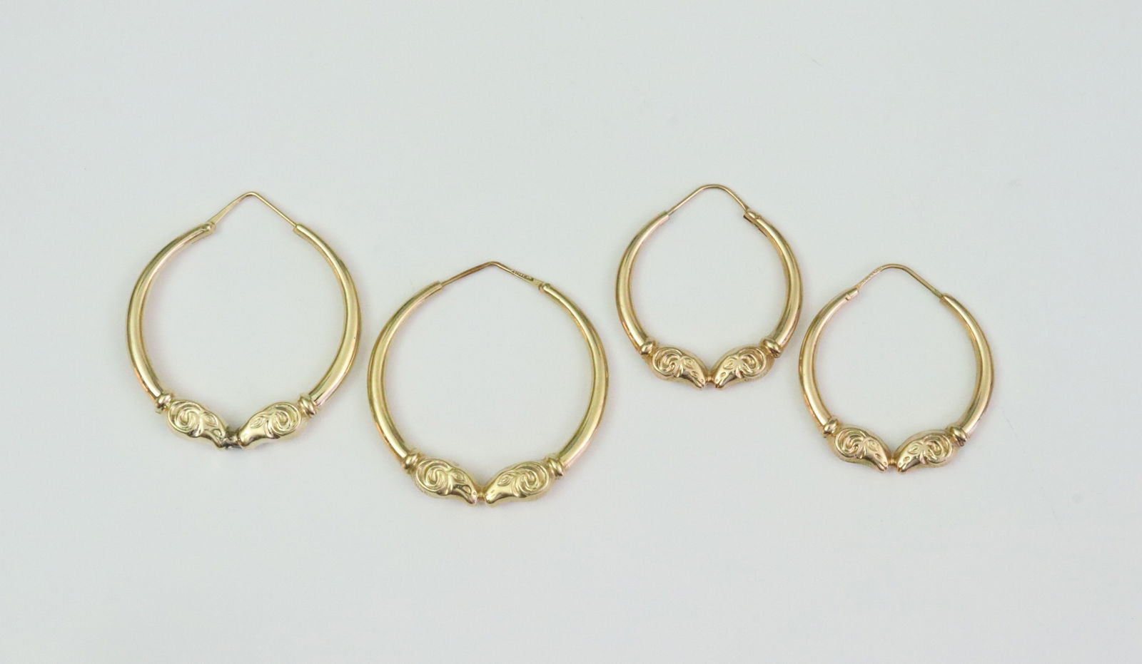 (2) PAIRS 18K HOLLOW GOLD RAMS HEAD HOOPS: each stamped 'Italy 18K', the larger pair with gold fissure defects and solder remnant where noses touch, 1.75in., the smaller pair 1.5in., gross weight 18.7gms., Opening Bid $1400