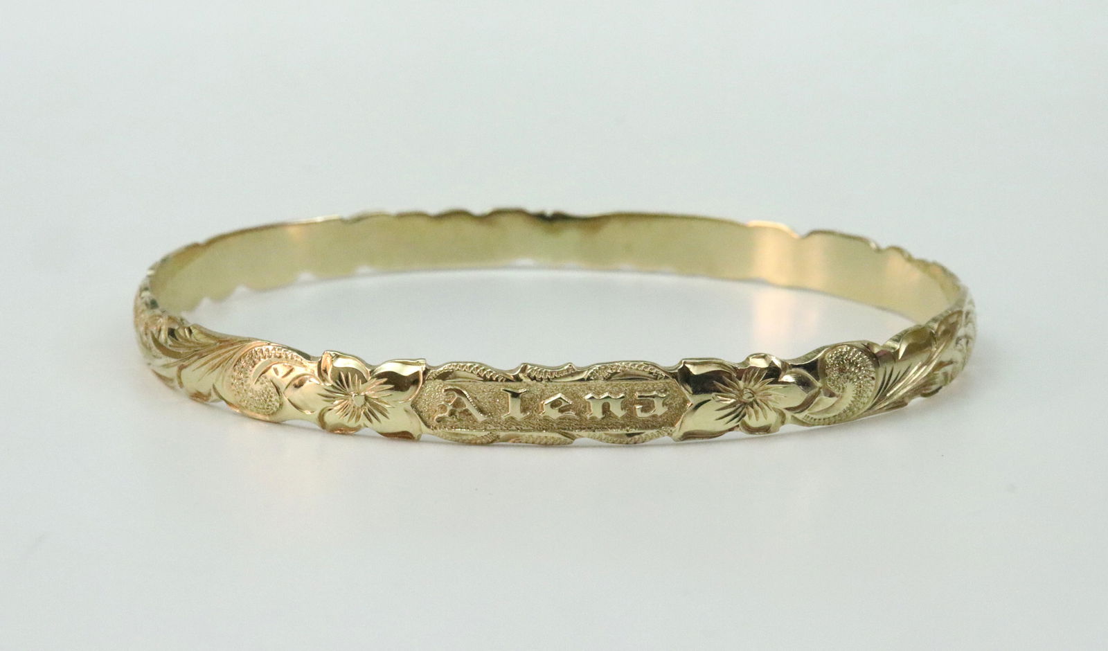 14K SLIP-ON BANGLE BRACELET: designed in carved waves, personalized 'Alena', interior engraved 'Hawaii 2004', in yellow gold, stamped 14K, width 5mm, inner circumference 7in., 14.4gms., Opening Bid $700