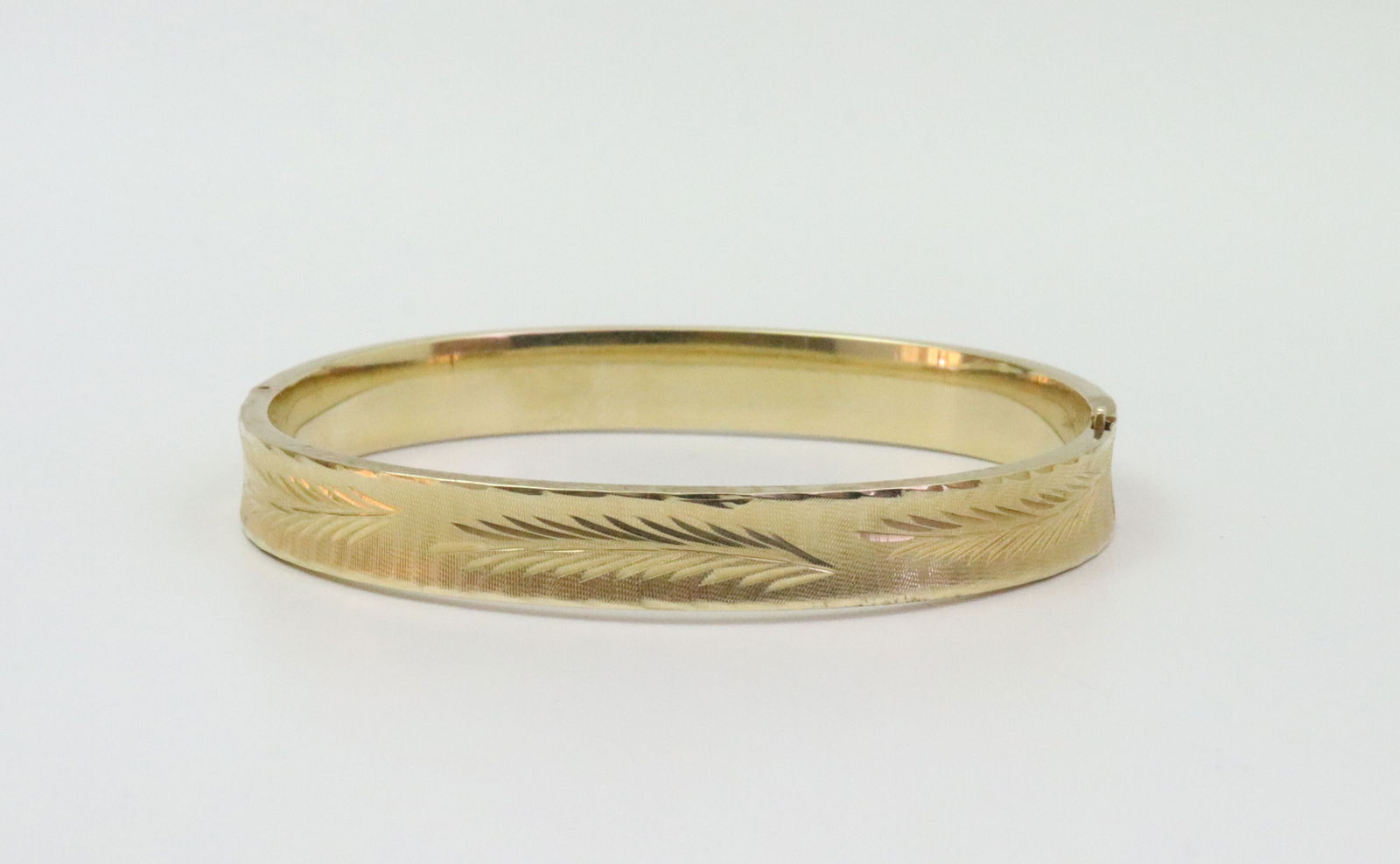 14K SLIDE HINGED BANGLE BRACELET: in yellow gold with bright-cut design, stamped 14K, width 8mm, inner circumference 6.5in., 12.8gms., Opening Bid $700