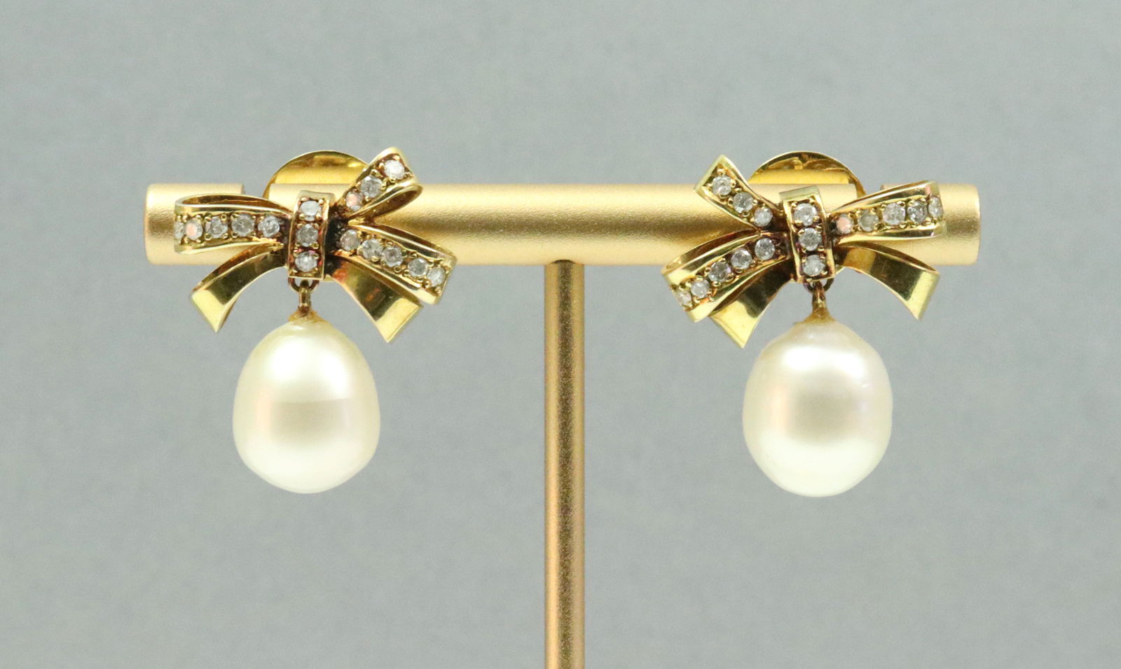 PAIR 14K DIAMOND BOW-FORM PEARL DROP EARRINGS: each bow suspending a (12mm) oval baroque pearl (some adhesive remnant at pearl attachments), total diamond weight for the pair 0.50ctw., in yellow gold, test 14K including earring backs, .9in.,