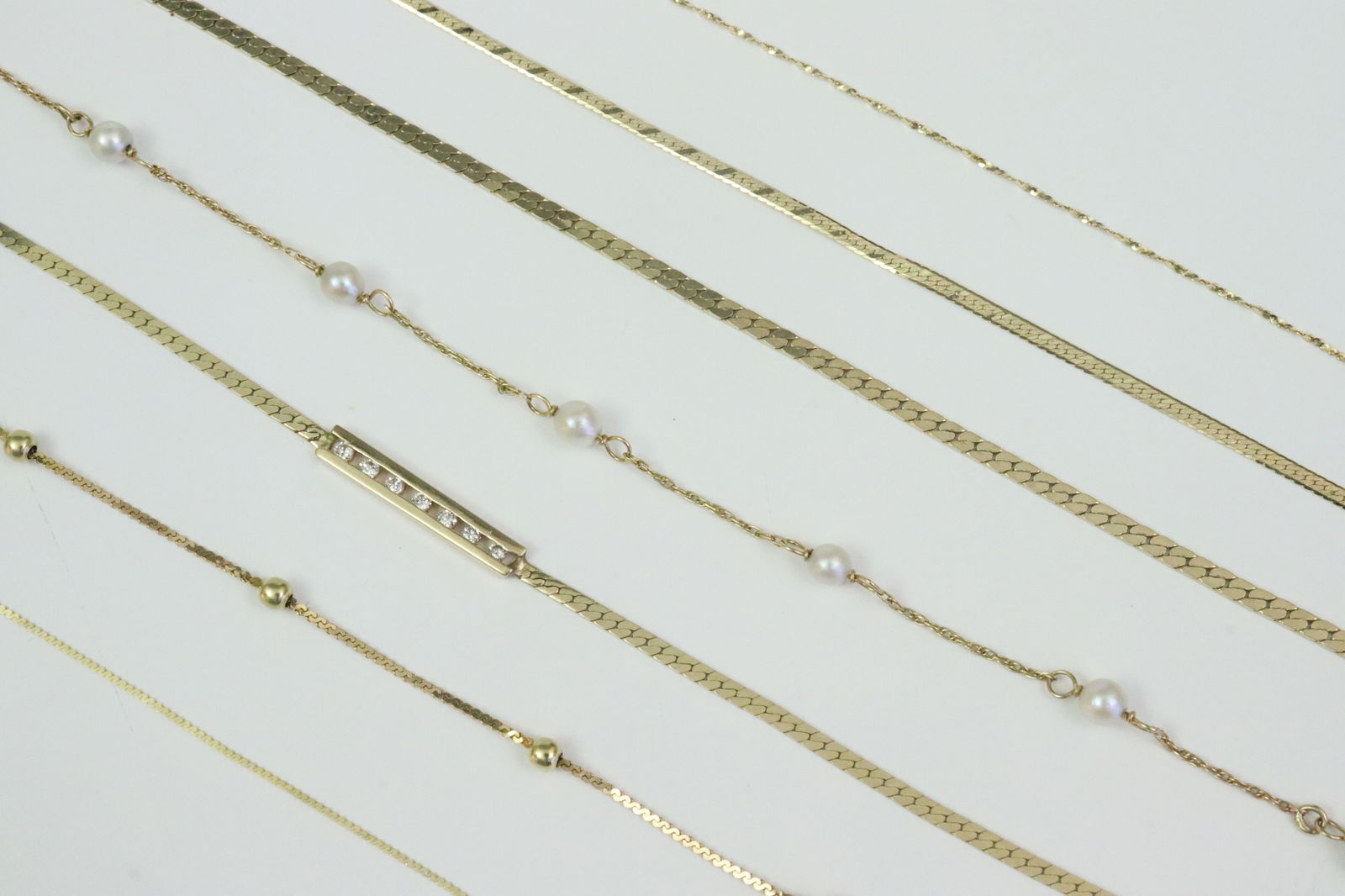 (7) PIECE 14K BRACELET & ANKLET GROUP: 5 chain link bracelets include a herringbone with 7 channel-set melee diamonds, a parallel link with 3.5mm cultured pearl stations, an Italian serpentine link with gold ball spacers, a herringbone lin
