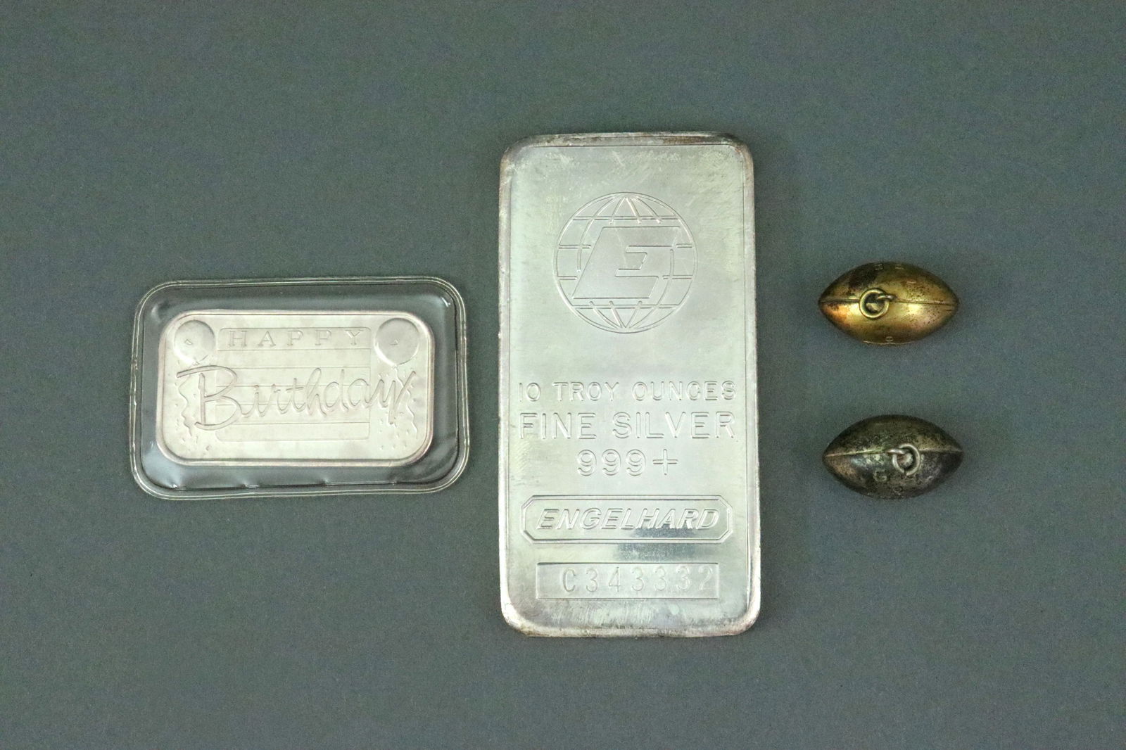 (4) PIECE SILVER GROUP INCL. SILVER BARS: including a 10 troy ounce 999+ fine silver bar, Engelhard #C343332, a one troy ounce .999 fine 1993 'Happy Birthday' bar (sealed), and 2 sterling football charms (.28ozt), each monogrammed, Opening
