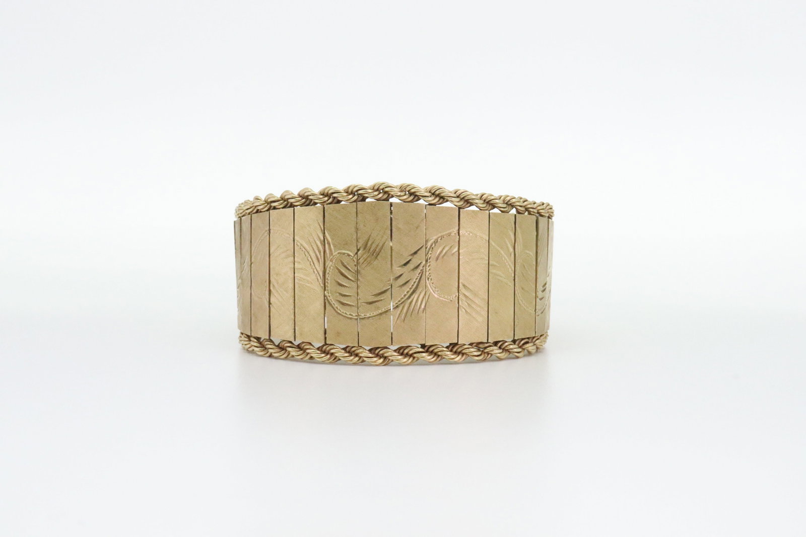 14K TAPERED PANEL LINK BRACELET: in bright-cut scroll design over articulated tapered panels of yellow textured gold with rope trim, overall width 28mm, length 6.5in., stamped 'OC14K', safety clasp, 44.3gms., Opening Bid $1900