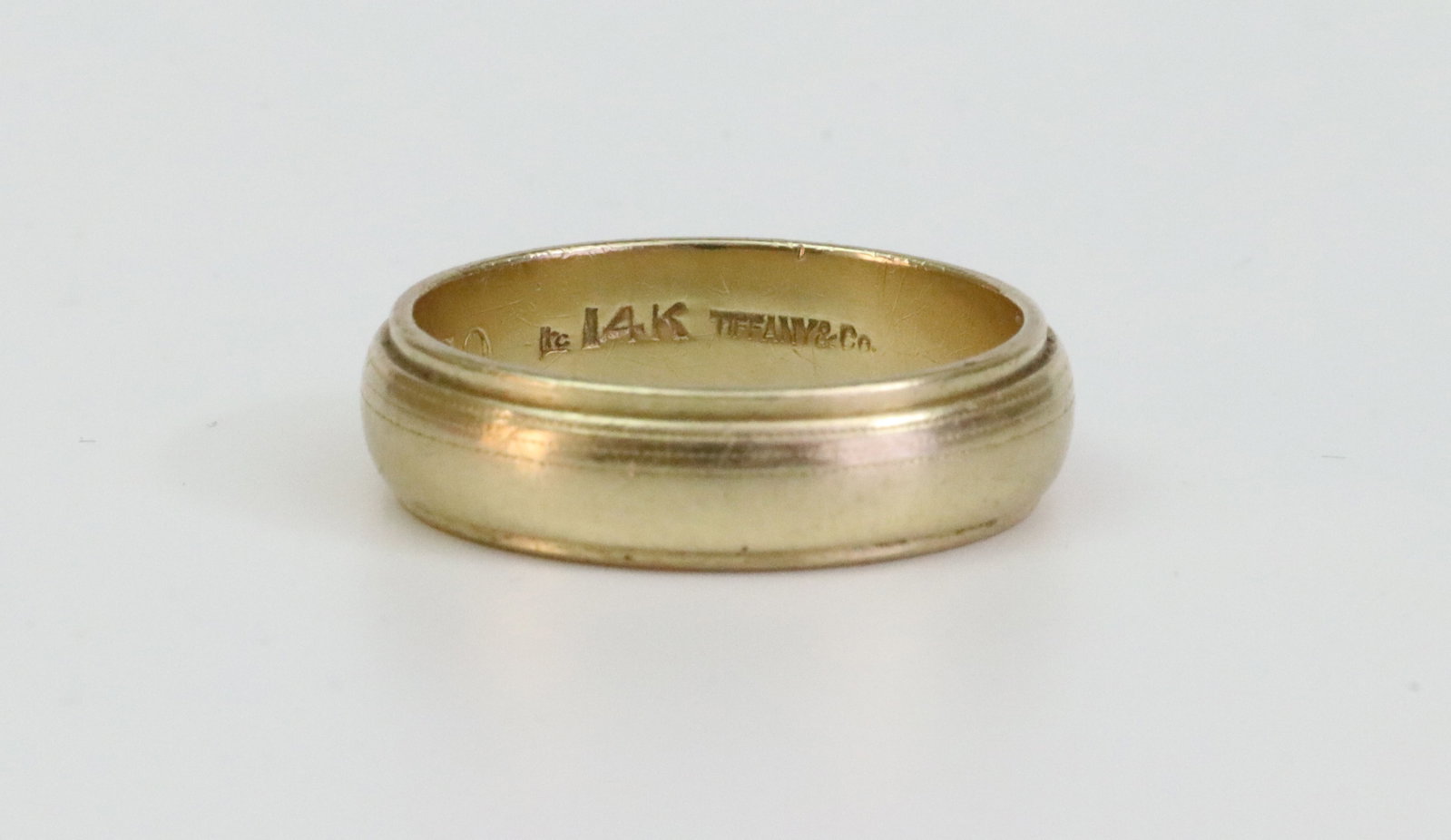 TIFFANY & CO. 14K GENTS WEDDING BAND: with carved beveled edges, in yellow gold, stamped 'Tiffany & Co. 14K', initialed interior dated '69, gold scratches, width 6mm, size 9, 6.3gms., Opening Bid $400