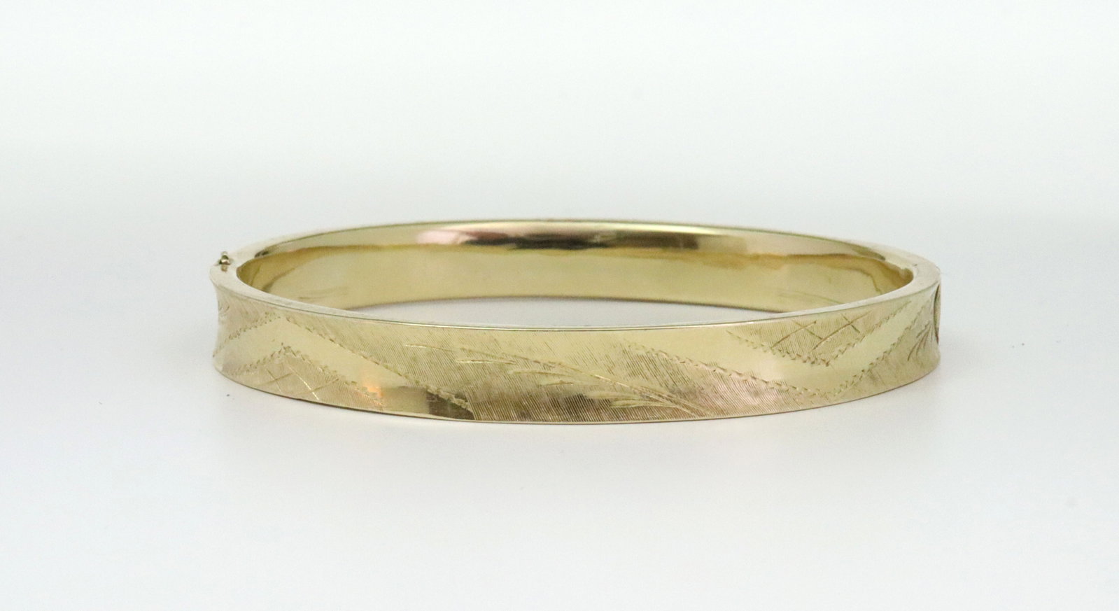 14K SIDE HINGED BANGLE: in yellow gold with bright-cut design (top and bottom face with some dings and shallow dents), tests 14K, width 8mm, inner circumference 7in., 13.4gms., Opening Bid $600