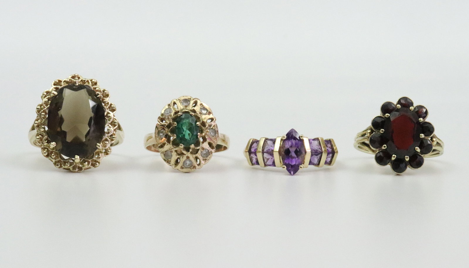 (4) 14K GEMSTONE RINGS: including an oval smoky quartz with filigree bead surround, overall 21x18mm, size 9, an oval garnet within a 10-stone garnet surround, stamped Germany, overall 17x13mm, size 7.5, an oval green spinel