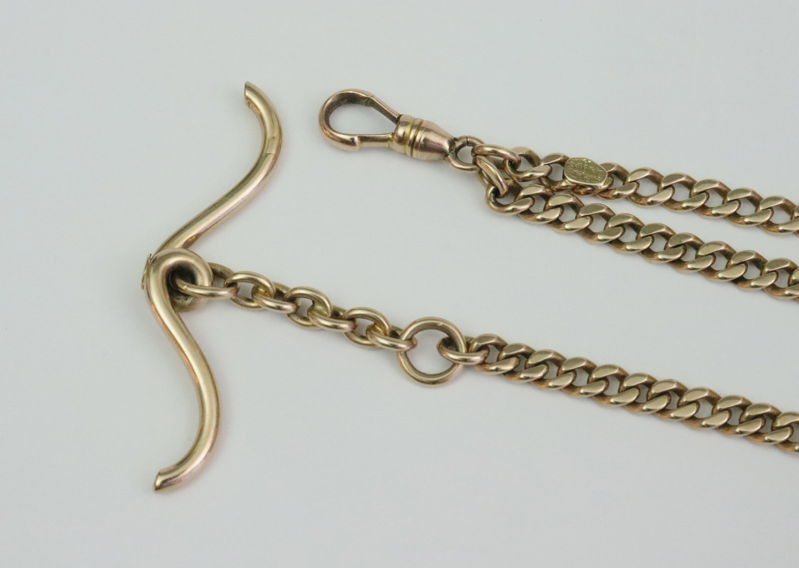 MJ PEIKES 14K WATCH CHAIN WITH NON-GOLD EXTENSION: the curb link chain overall measures 35", all elements of first 22.5" test 14K including chain, T bar, dog clip clasp, and gold tag stamped 'MJ Peikes 14K', the remaining 12.5" extension chain