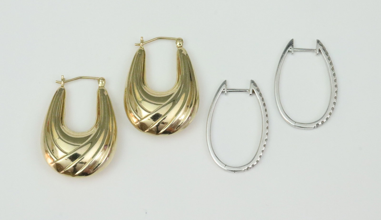 (2) PAIRS OF OVAL HOOP EARRINGS: including a pair of white gold hoops each set with 17 round natural diamonds, total diamond weight for the pair approx. 0.34ctw, and a pair of yellow hollow gold puffy hoops in drape design, each stam