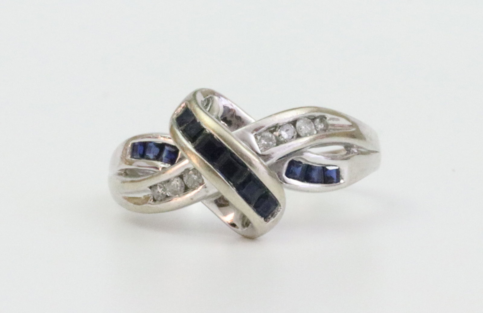 14K SAPPHIRE & DIAMOND CROSSOVER RING: set with 12 caliber cut sapphires approx. 0.50ctw, and 7 channel-set diamonds approx. 0.12ctw, overall ring head 12x18mm, in white gold, stamped 14K, size 7, 5.3gms. Note: Leighton makes no claims or