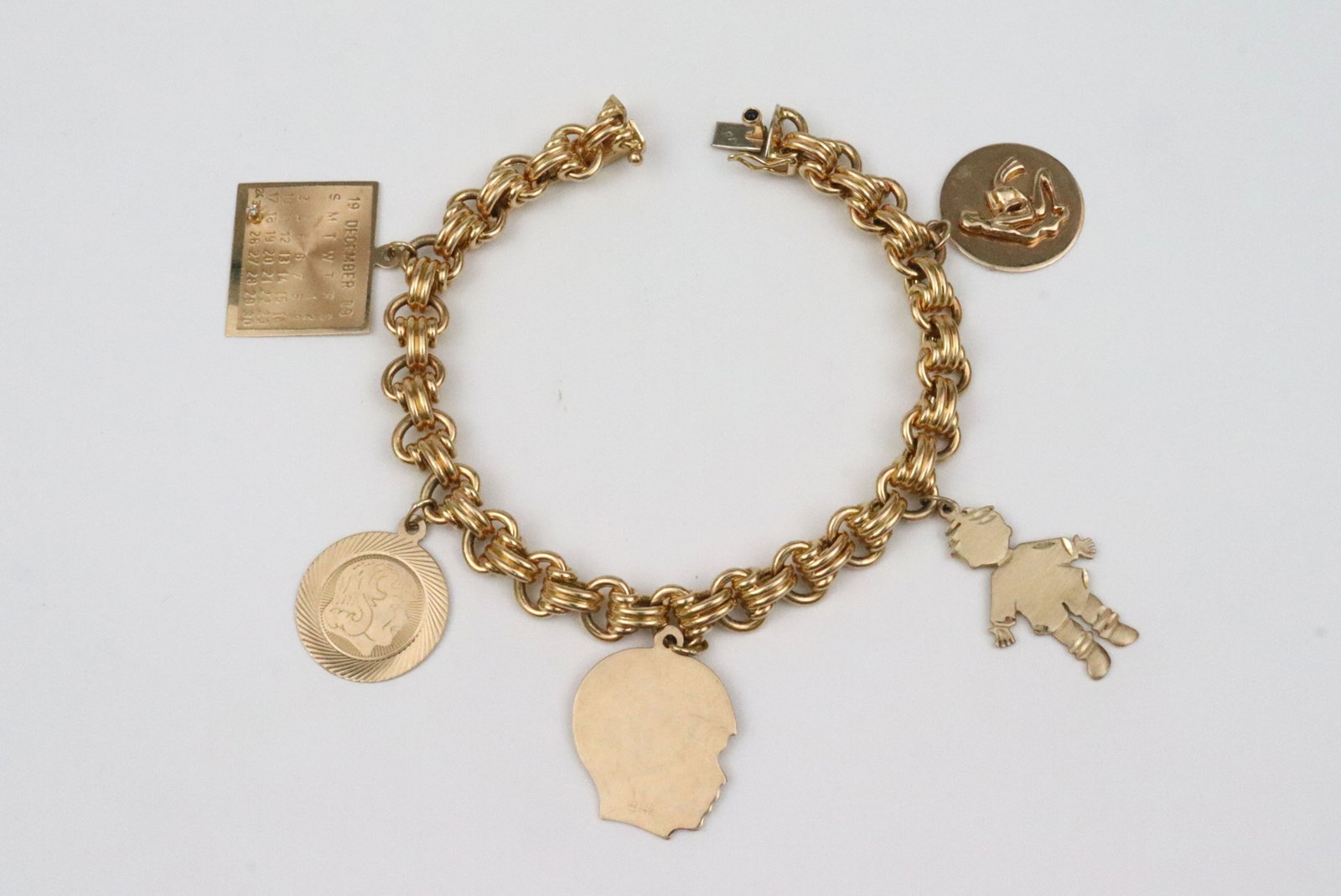 18K FRENCH CHARM BRACELET BY CAPLAIN PARIS: with (5) 14K charms including 2 silhouette profiles, a child figural, an Aquarius water bearer charm, and a 1989 calendar with diamond marker at Dec. 25, charms all stamped or tested 14K, bracelet