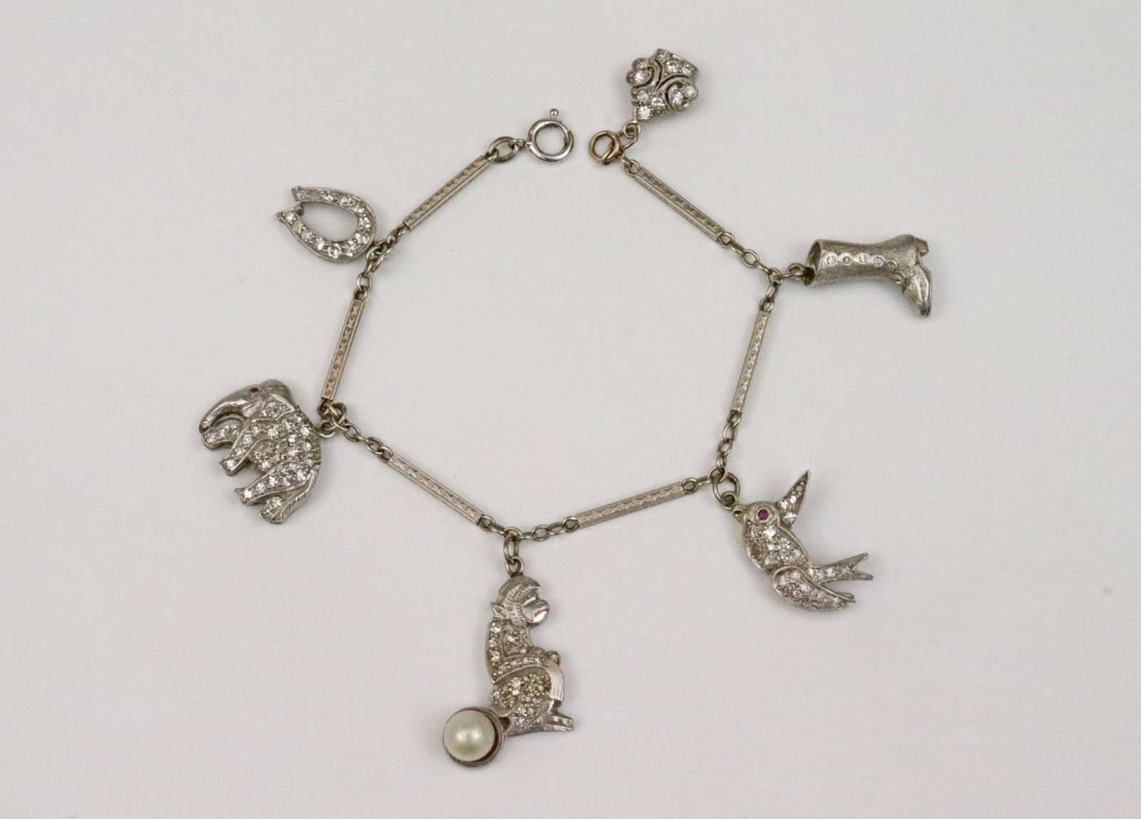 14K BAR LINK CHARM BRACELET WITH 6 PLATINUM CHARMS: comprising 5 diamond encrusted charms including a horseshoe, an elephant with ruby eye, a monkey with pearl, a bird with ruby eye, and a heraldic motif charm, and a high button boot with diamond
