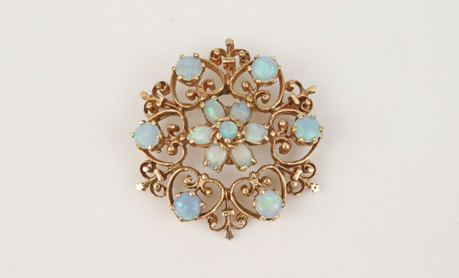 14K OPAL FILIGREE BROOCH: in scrollwork design, set with 13 opal cabochons, largest opals 4.5mm, in yellow gold, stamped 'GW 14K', overall diameter 1.3in., 9.9gms., Opening Bid $400