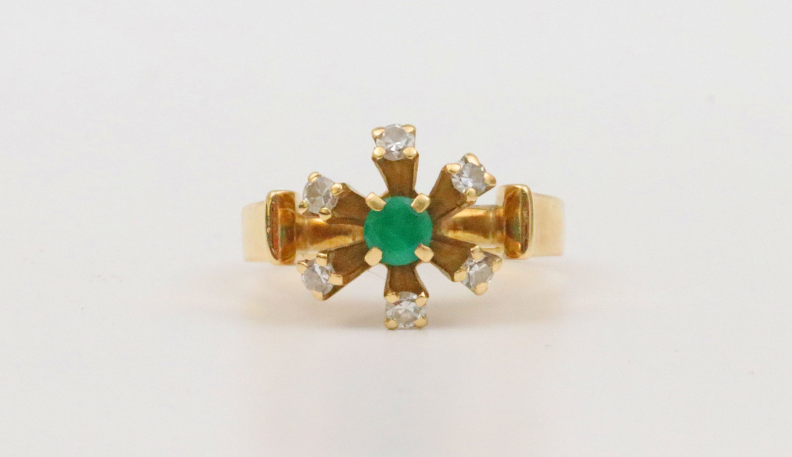 18K DIAMOND & EMERALD RING: in modern starburst design set with a central round emerald approx. 0.25ct, and 6 round natural diamonds approx. 0.24ct, overall head 11x15mm, in yellow gold, stamped '18K Fluhler' (likely Norbert