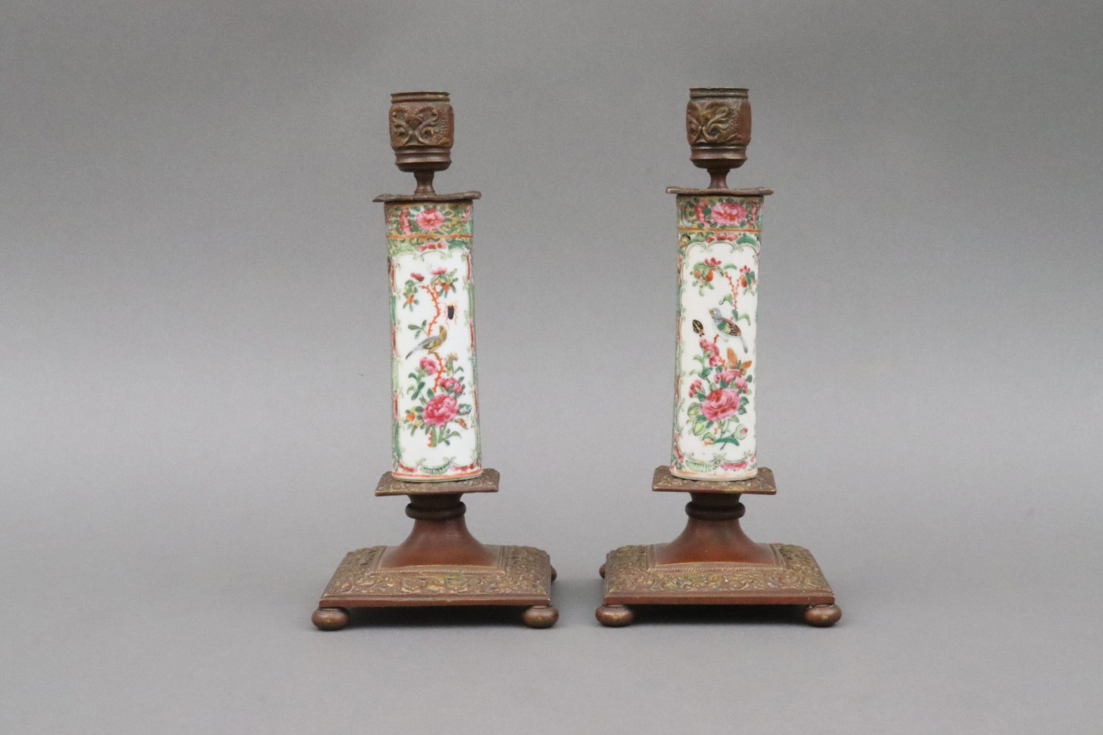 PAIR BRASS-MOUNTED ROSE CANTON CANDLESTICKS: likely 19thC., in famille rose bird and insect motif, brass with dark brown patination, raised on bun feet, brass base with a couple minor nicks and dimples, 10in.