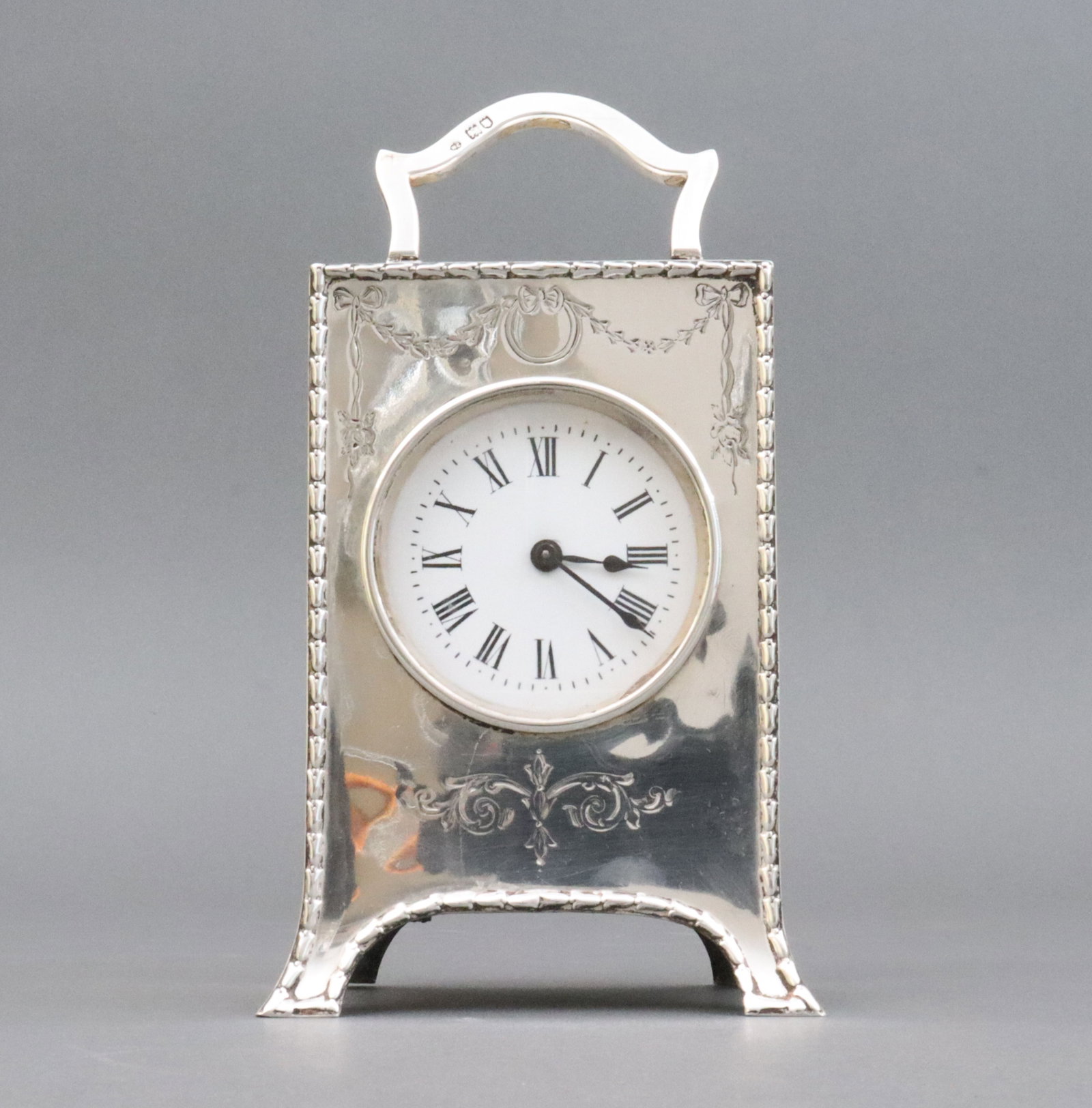 WILLIAM COMYNS BRITISH STERLING BOUDOIR CLOCK: the front panel in floral swag and scroll motif, on bracket feet, swing carry handle, marks for London, sterling, 1926 and Comyns, French movement, the clock is currently running, however not