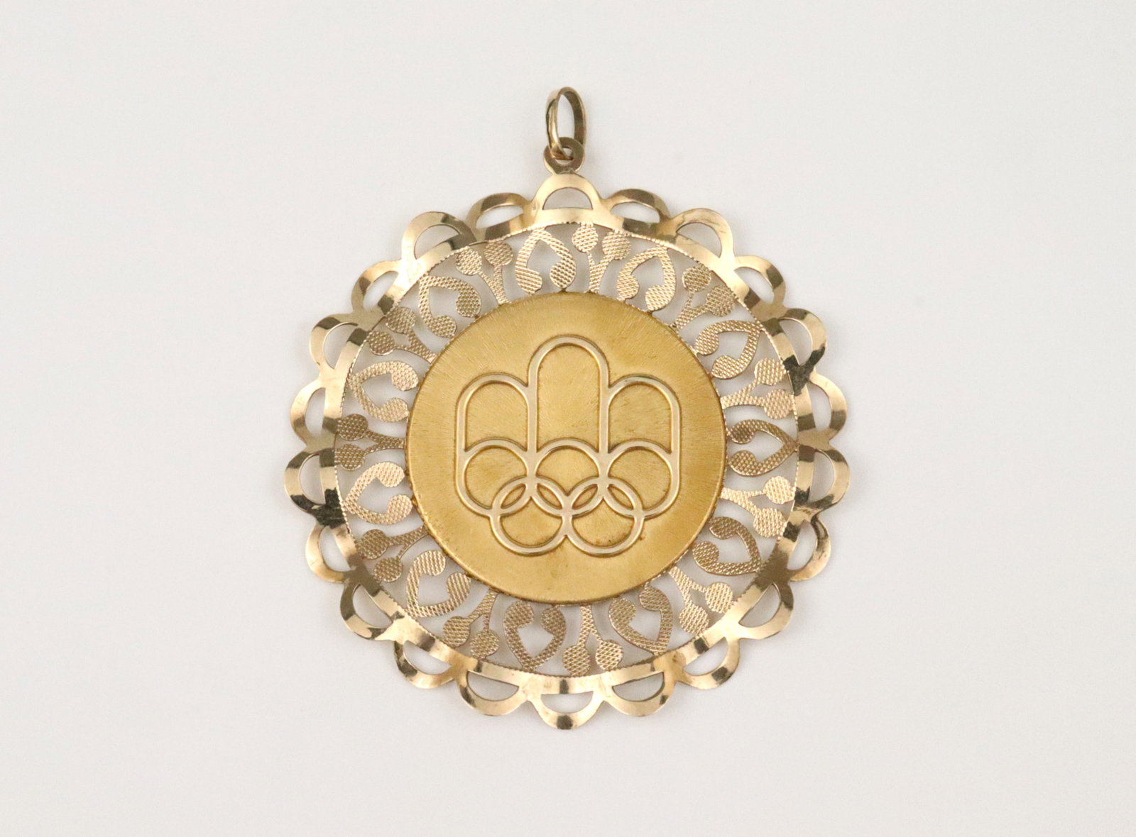 10K LARGE 1976 MONTREAL OLYMPIC FILIGREE PENDANT: depicting the official graphic emblem of the 1976 Montreal games, in yellow gold (verso well-scratched), stamped '1972 COJO 76 DUO ISJC 10K', 2.25in., 12.2gms., Opening Bid $300