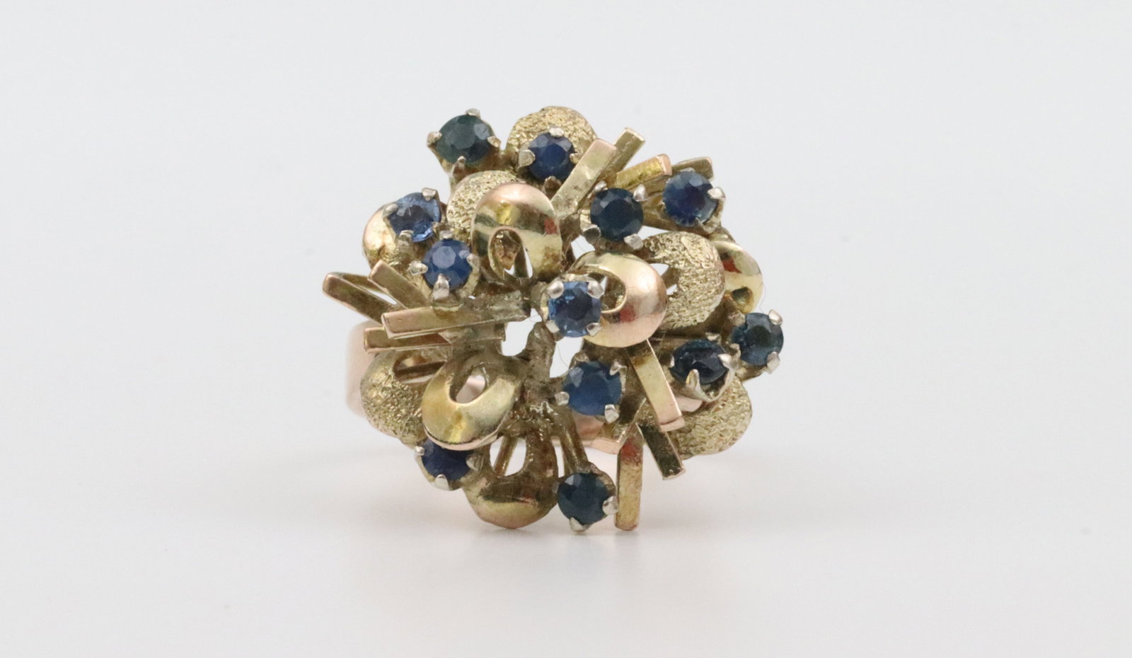 10K SAPPHIRE CLUSTER RING: set with 12 round sapphires approx. 0.80ctw, overall ring head 22x23mm (appears to be a structural loss from the cluster arrangement), in yellow textured and polished gold, tests 10K (stamped 14K),