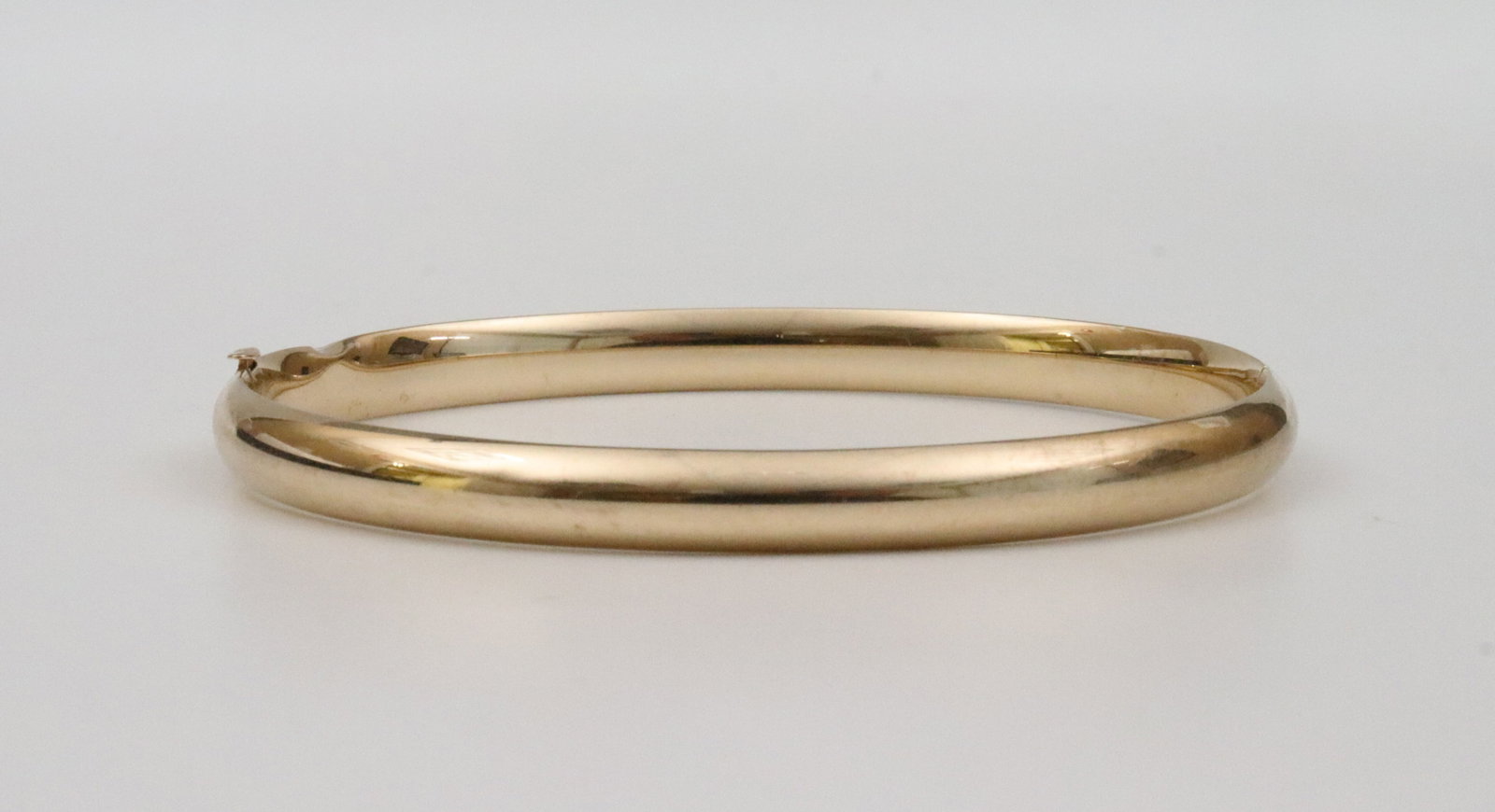 ETERNAGOLD 14K SLIDE HINGED BANGLE: in yellow gold, stamped '14K Costa Rica', and with EG maker's mark, edge dent, width 5.5mm, inner circumference 7-7.5in., 6.4gms., Opening Bid $300