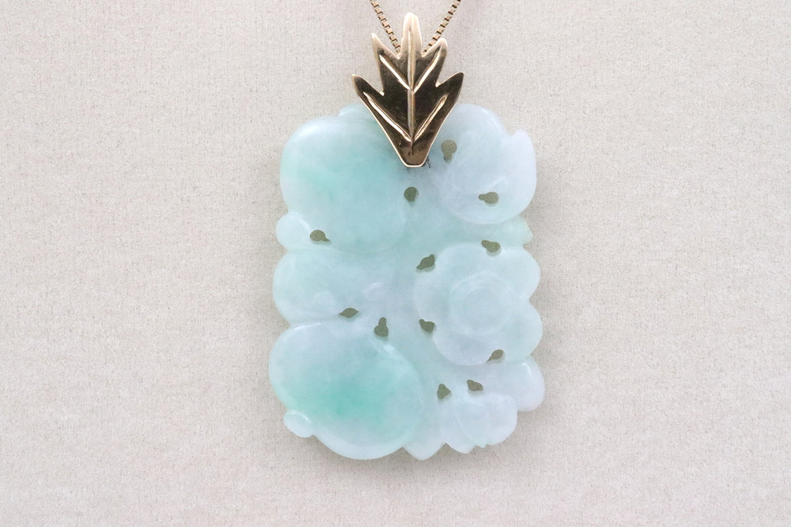 14K CHINESE CARVED JADE PENDANT ON CHAIN: in apple green with subtle variegation, designed in pierced floral and fruit motif, with gold-mounted articulated leaf-form bale, tests 14K, width 1.3in., overall length 2.2in., 15gms., on box link ne