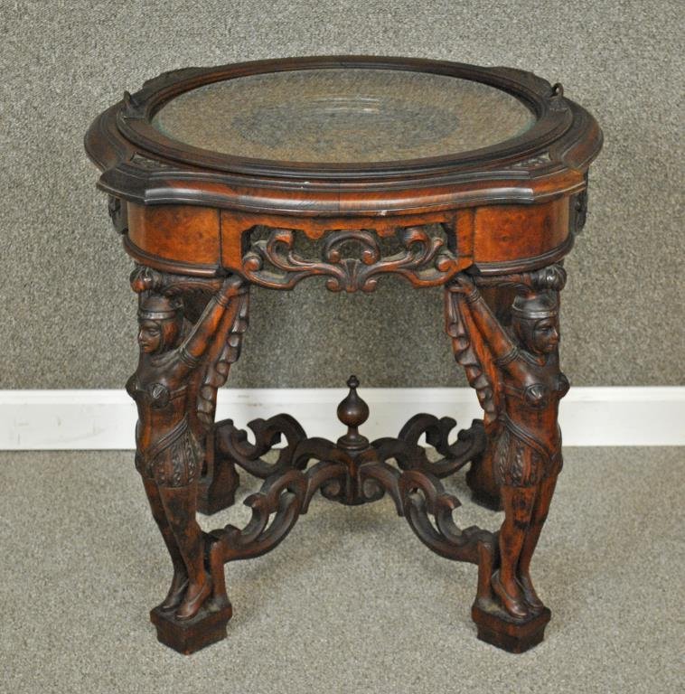 CARVED EGYPTIAN REVIVAL-STYLE TRAY TOP TABLE: with walnut and mahogany woods, beveled glass tray top opening to carved profile figures, caryatid figural legs, cross stretchers with center finial, 23x25in.