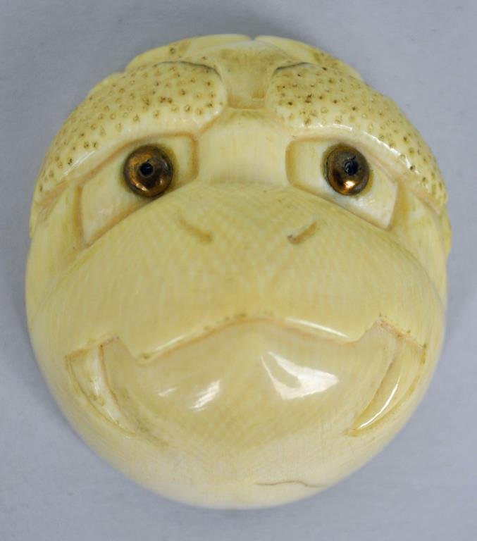 CARVED IVORY NETSUKE OF A STYLIZED MONKEY FACE: brass inset eyes, 2x1.75in., Estate Collection