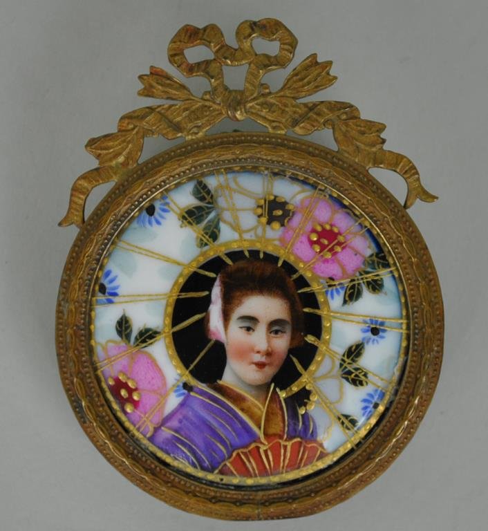 FRAMED PORTRAIT MINIATURE OF A GEISHA: circular porcelain plaque hand painted over transfer, in ribbon crested easel-back frame, plaque diameter 2.25in., Estate Collection