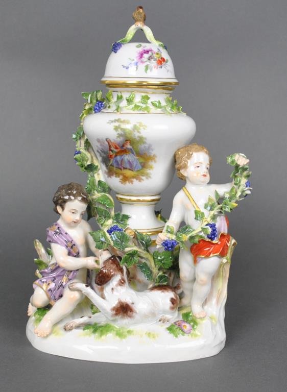 MEISSEN (AS IS) FIGURAL COVERED URN: with putti and dog in a garden setting, lid with bird finial, underglaze blue cross swords mark, impressed ‘1009/125’, significant losses to foliage, small pieces retained for restoration, 11x7.5i