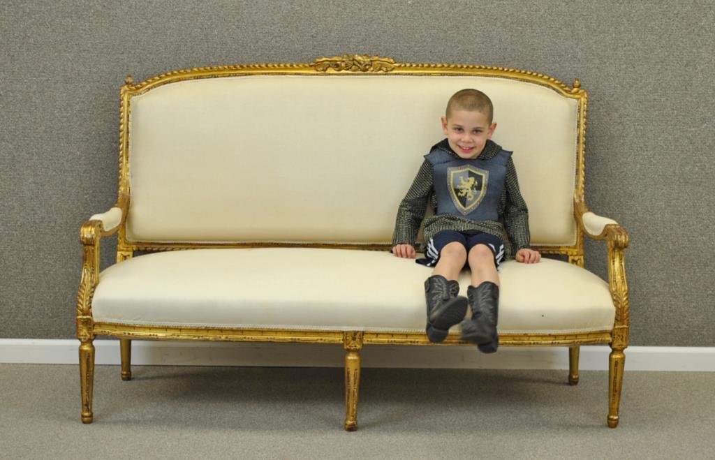 LOUIS XVI-STYLE GILTWOOD SETTEE: 19th/20thC., large settee with carved frame and crest, foliate and acanthus carved arms, raised on 5 fluted tapering circular legs, cream colored upholstery (soiled), wood repairs to arms, gilt losses