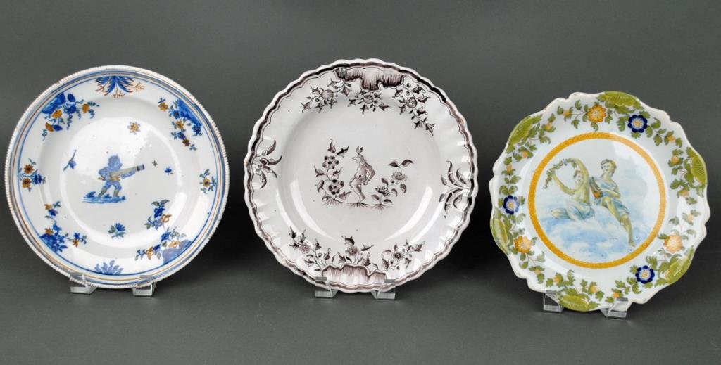 (3) FRENCH FAIENCE FIGURAL PLATES: 18th/19thC., including a manganese soup plate with a grotesque amidst florals, an underglaze decorated plate depicting a grotesque with canon, and a plate depicting allegorical figures, GM mark to und