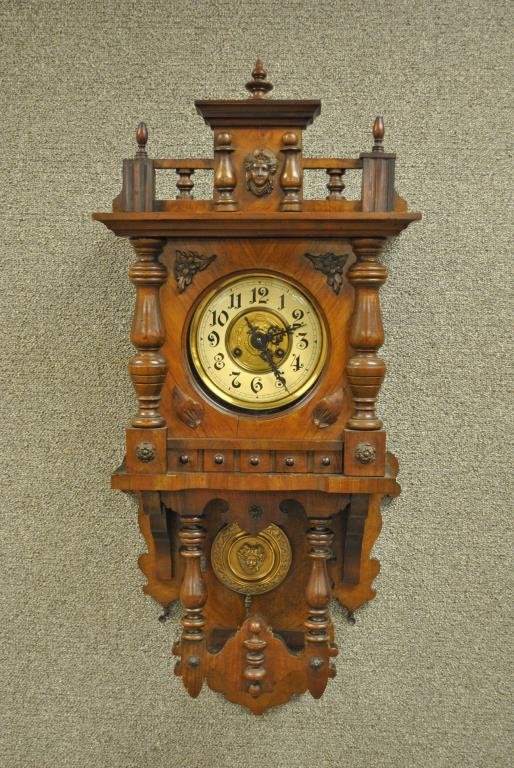 GERMAN CARVED WALNUT WALL CLOCK: 19thC., unknown maker, the pediment with applied female mask, allover applied leaf and floral decoration (one leaf appears to be restored), brass female mask pendulum, 35x14in.