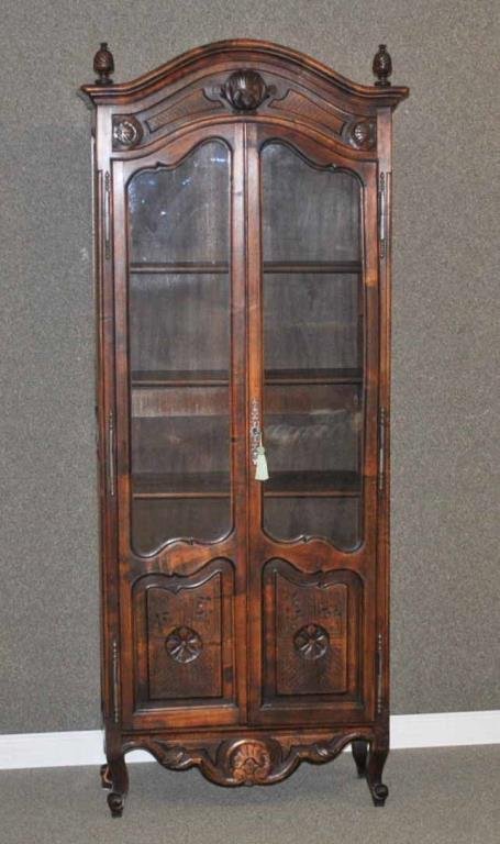 COUNTRY FRENCH-STYLE WALNUT CABINET: two-door, with foliate and shell carvings, pineapple finials, glazed doors, 68x28x12in., repair to left rear leg