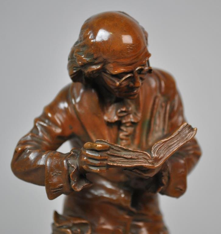 CARL KAUBA (American / Austrian 1865-1922): bronze sculpture of a bespectacled man paging through a book, with more books in his pocket and between his knees, signed on plinth side, impressed 'Geschutzt 4158' on coat back, marble base, bronze 9
