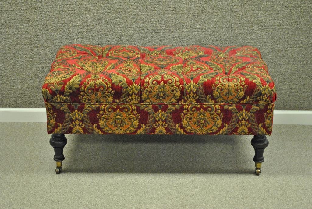 UPHOLSTERD LIFT-TOP STORAGE BENCH: in red and gold fabric, hinged opening, wood legs with metal wheels, 20x43x24in.