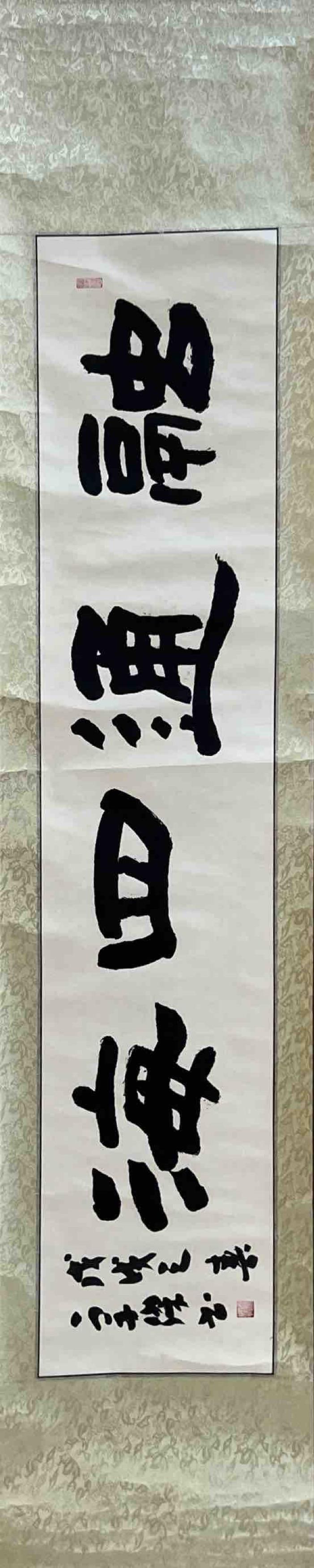 TRADITIONAL CHINESE CALLIGRAPHY SCROLL: TRADITIONAL CHINESE CALLIGRAPHY SCROLL A VERTICAL SCROLL FEATURING BOLD BLACK INK CHINESE CALLIGRAPHY CHARACTERS WRITTEN IN A CLASSIC BRUSH STYLE, MOUNTED ON A DECORATIVE BACKING. THE CHARACTERS ARE L