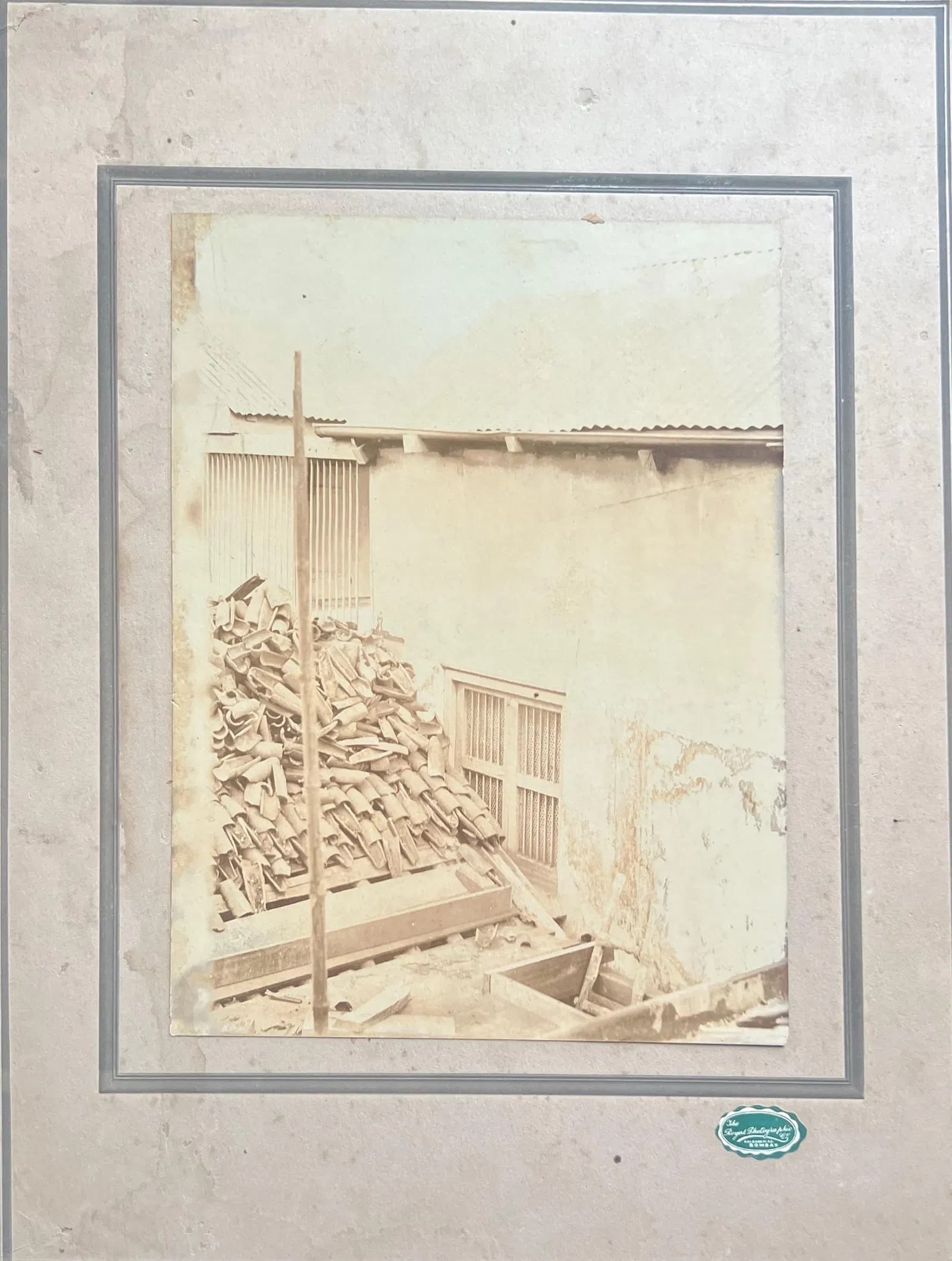OLD SEPIA PHOTOGRAPH OF A WORKSITE WITH PILED MATERIALS: OLD SEPIA PHOTOGRAPH OF A WORKSITE WITH PILED MATERIALSA FADED, VINTAGE SEPIA-TONED PHOTOGRAPH CAPTURING A SIMPLE OUTDOOR WORK AREA BESIDE A WEATHERED BUILDING. A TALL STACK OF TILES OR ROOFING